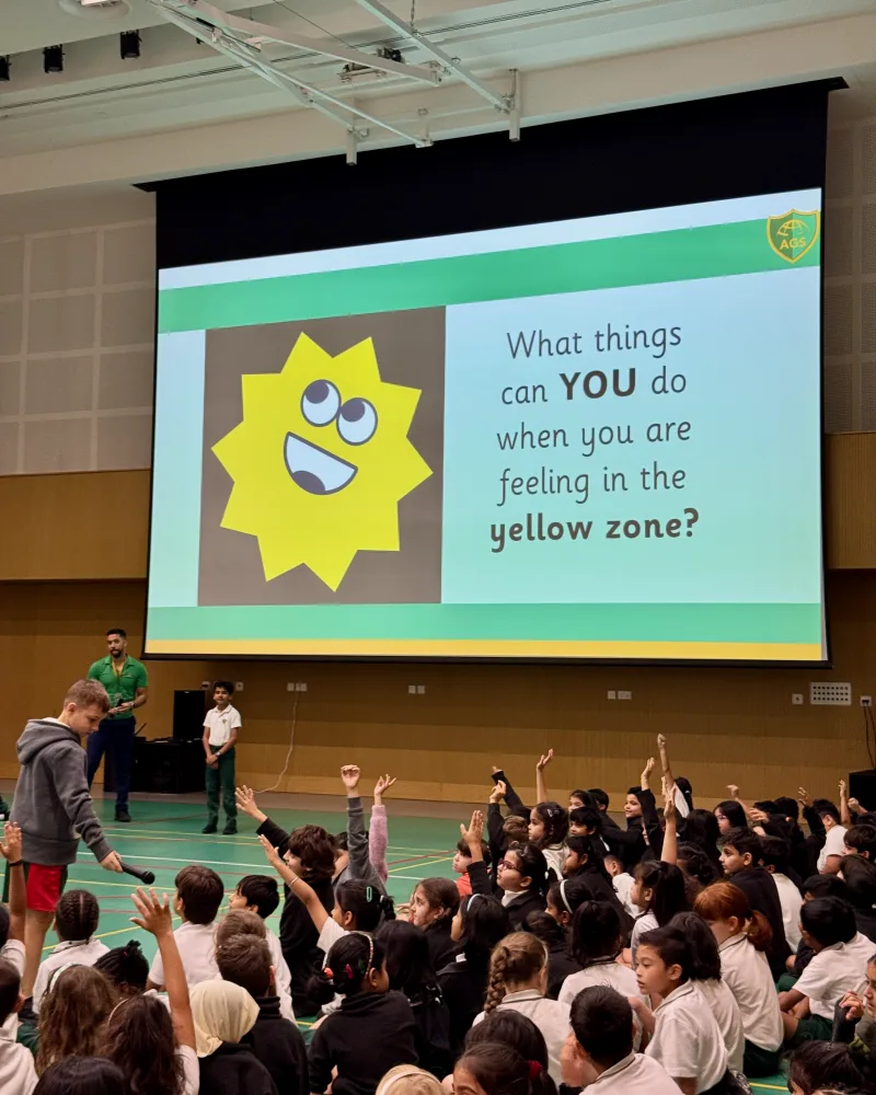 Arcadia Global School students raising their hands in an assembly, in front of a slide asking what they can do when they are feeling in the yellow zone