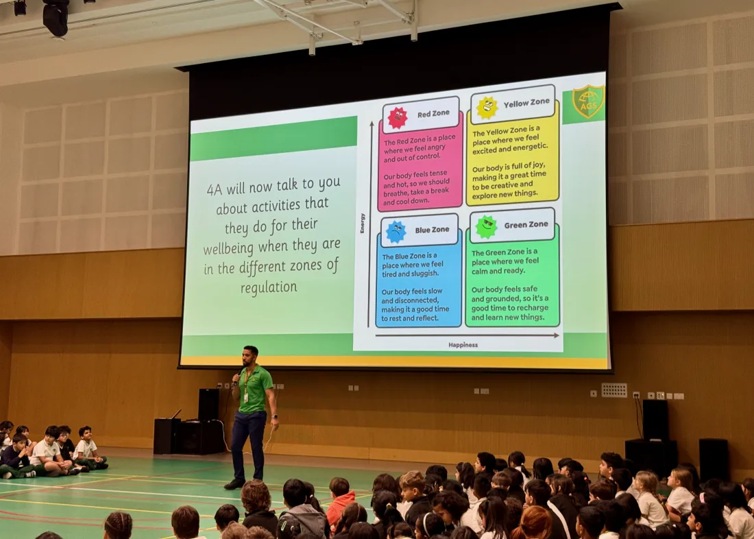 A teacher leading an Arcadia Global School assembly in front of a slide showing the red, yellow, blue and green quadrants of the mood meter